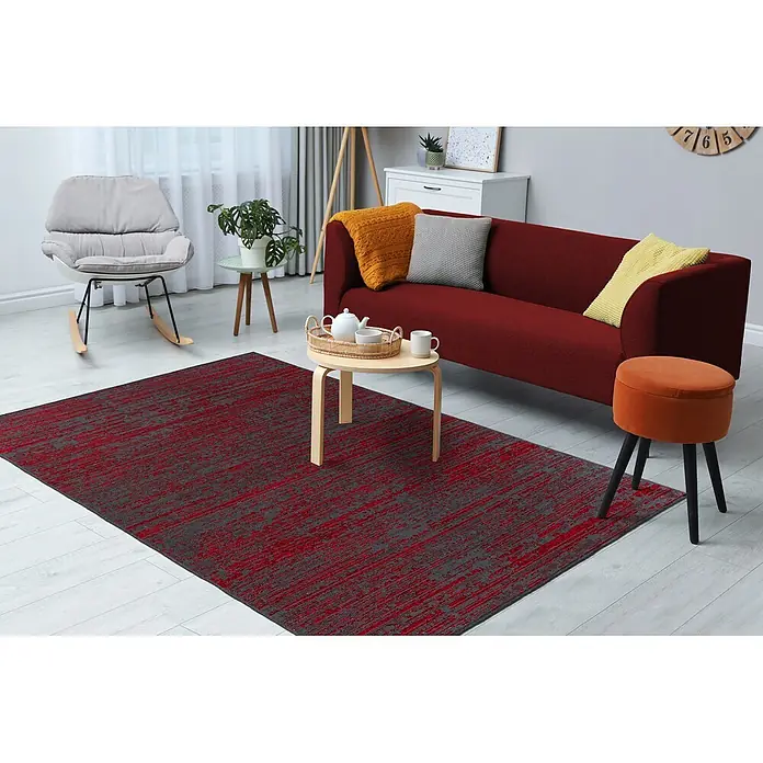 Kayoom Flachgewebeteppich Kalea 125 - Rot, 170 x 120 cm, 100 % Polyester - Ein rot-grauer Teppich mit abstraktem Muster auf hellem Holzboden in einem modernen Wohnzimmer.
