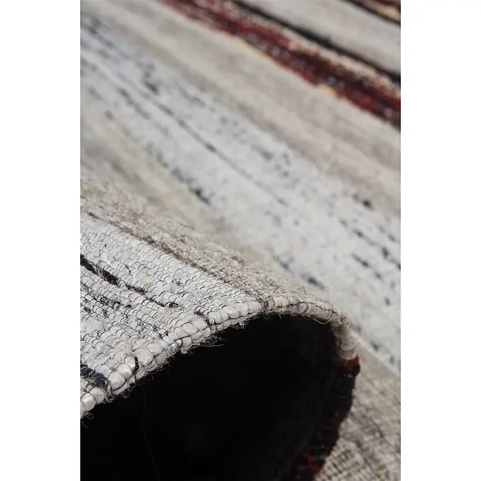Kayoom Flachgewebeteppich Duarte 210 - Schwarz/Weiß, 230 x 160 cm, 60 % Wolle, 20 % Baumwolle, 20 % Seide - Nahaufnahme eines teilweise aufgerollten, hellgrauen und weißen Webteppichs mit dunklen und roten Akzenten.