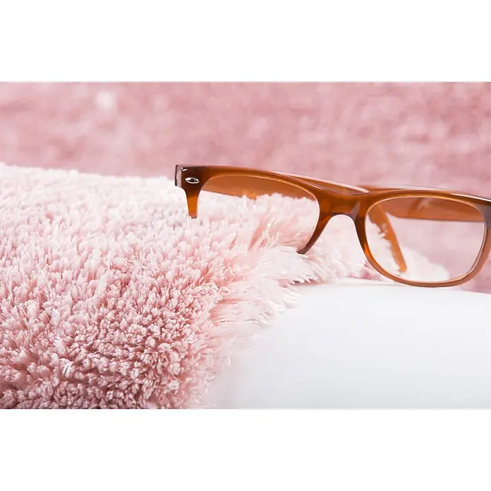 Kayoom Hochflorteppich Dolphin 500 - Rosa, 290 x 200 cm, 100 % Polyester - Braun umrandete Brille liegt auf flauschiger rosa Decke, mit unscharfem rosa Hintergrund.