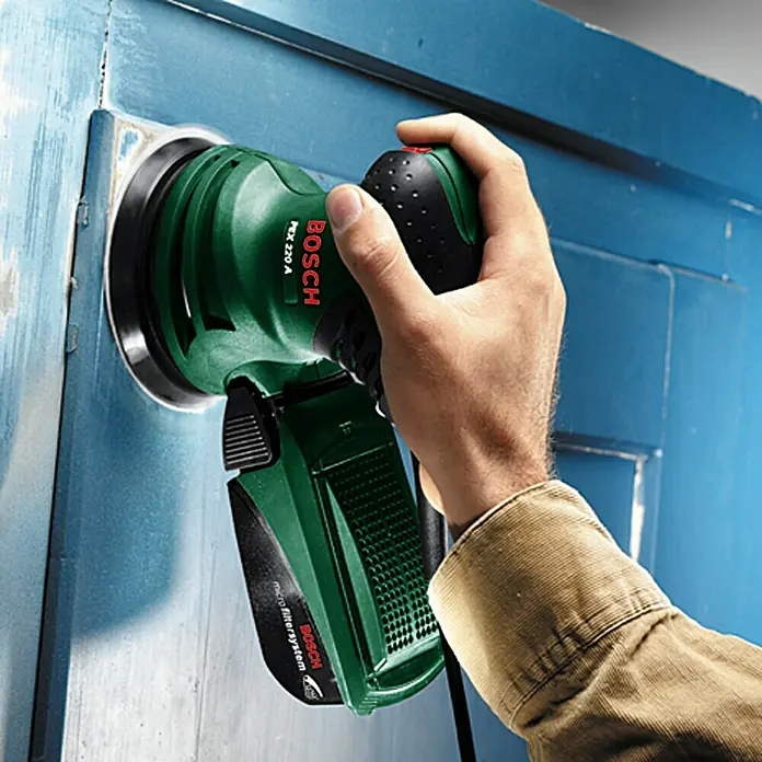 Bosch Elektro-Exzenterschleifer PEX 220 A - 220 W, Durchmesser Schleifteller: 125 mm - Bosch PEX 220 A Exzenterschleifer bei der Arbeit an einer blauen Tür. Das Gerät ist grün und wird von einer Hand bedient.
