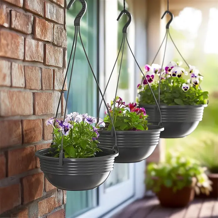 Plastard Blumenampel 3er Set Ø 25 cm in Anthrazit mit Aufhänger, Deko Blumentopf - 3 Stk., Außenmaß (Ø x H): 25 x 10 cm, Kunststoff, Anthrazit - Drei dunkelgraue Hängepflanzer mit bunten Blumen, draußen an einer Ziegelwand und Glastür hängend.