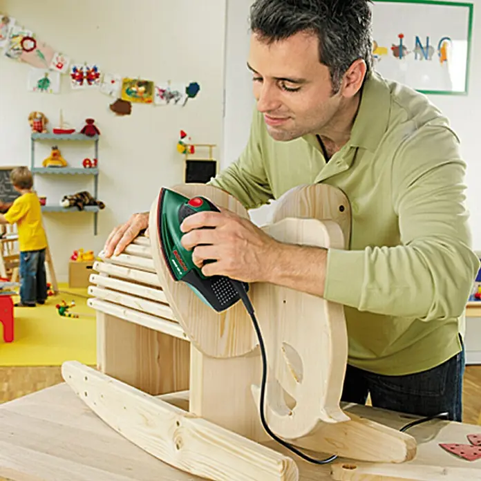 Bosch Easy Lijadora multifunción eléctrica  PSM 80 A - 80 W, Número de oscilaciones marcha en vacío: 22.000 r.p.m., Diámetro circuito oscilante: 1,4 mm - Un hombre lija un caballo de madera con una lijadora multifunción verde Bosch. La herramienta es compacta y de diseño ergonómico.