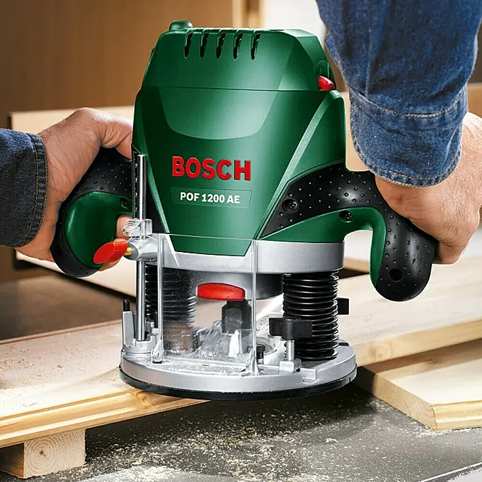 Bosch Fresadora eléctrica POF 1200 AE - 1.200 W, 11.000 r.p.m. - 28.000 r.p.m., Diámetro del portaherramientas: 6 mm - 8 mm - Primer plano de una fresadora Bosch POF 1200 AE en acción, trabajando la madera y ofreciendo resultados precisos.\n