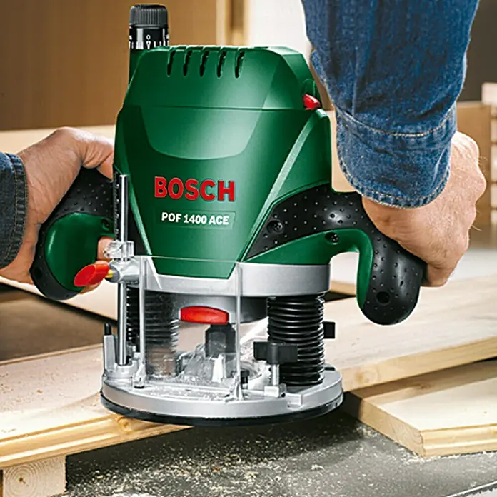 Bosch Fresadora eléctrica POF 1400 ACE - 1.400 W, 11.000 r.p.m. - 28.000 r.p.m., Diámetro del portaherramientas: 6 mm - 8 mm - Imagen de una fresadora Bosch POF 1400 ACE en acción, sujetada por dos manos trabajando la madera.