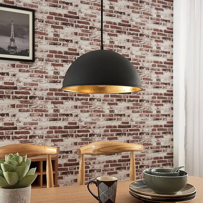 Lindby Pendelleuchte Leya - schwarz, Schwarz, gold, E27 - Schwarze Pendelleuchte mit goldenem Inneren über einem Esstisch in einem Raum mit Ziegelwand.