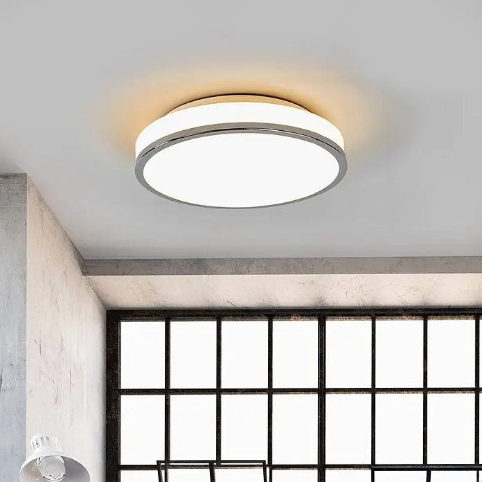 Lindby LED Deckenlampe in weiß, chrom, Deckenleuchte rund -  - Moderne runde LED-Deckenleuchte mit Chromrahmen, die einen Raum mit Betonwänden und großem Fenster beleuchtet.