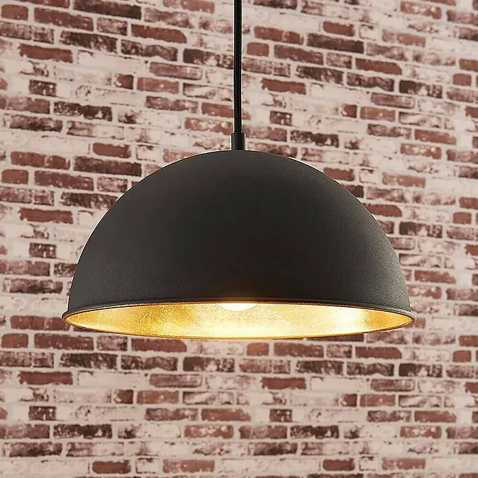 Lindby Pendelleuchte Leya - schwarz, Schwarz, gold, E27 - Schwarze Hängelampe mit goldener Innenseite, hängt an schwarzem Kabel vor einer Ziegelwand.