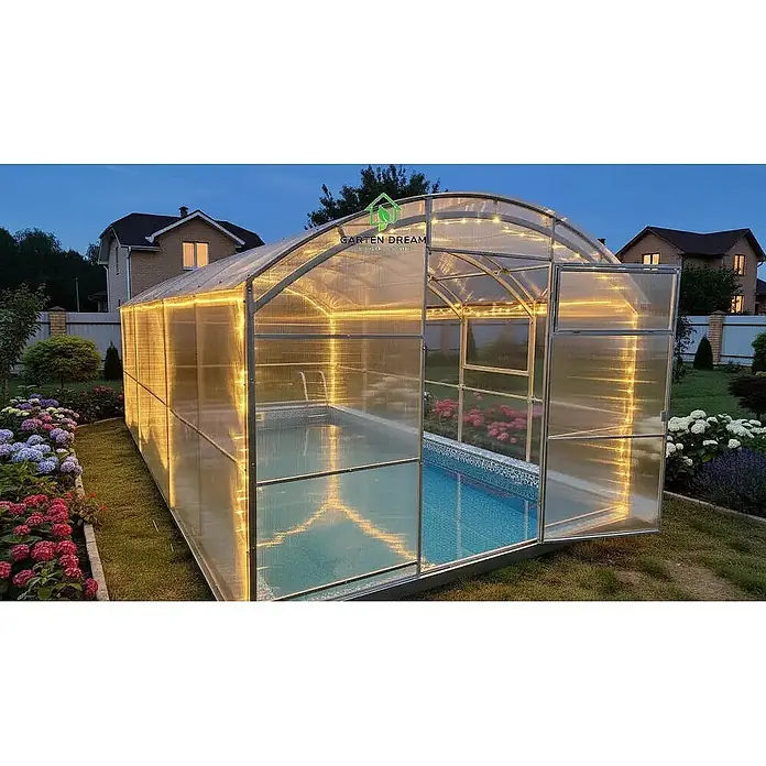 Garten Dream Poolüberdachung Poseidon, 6mm Polycarbonat - Passend für: Aufstellpools und eingelassene Pools, L x B x H: 800 x 300 x 215 cm - Eine transparente Gewächshaus-Poolüberdachung mit Metallrahmen und Lichterketten, die einen Pool im Garten bei Dämmerung bedeckt.