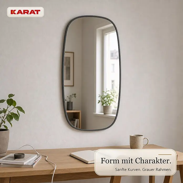 Floordirekt Wandspiegel Alina - 55,1 x 90,1 cm - Ein eleganter ovaler Spiegel mit schwarzem Rahmen hängt über einem Holztisch und reflektiert Fenster und Pflanzen.