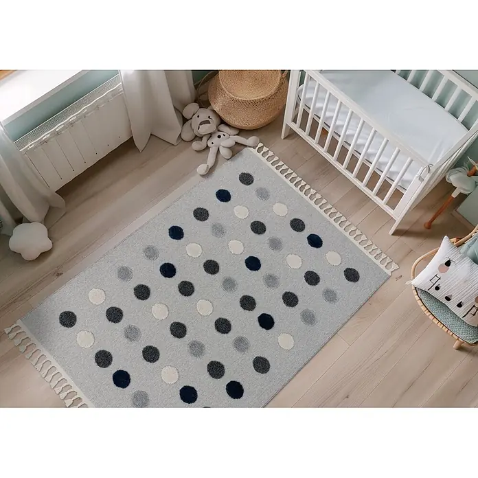 Kayoom Kinderteppich Modena 419 - Grau, 170 x 120 cm, 100 % Polypropylen - Hellgrauer Teppich mit dunkelblauen, grauen und cremeweißen Tupfen und Quasten auf Holzfußboden im Kinderzimmer.