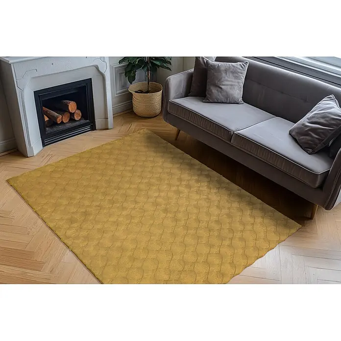 Kayoom Fellteppich Royal Glow 825 - Honig, 170 x 120 cm, 80 % Polyester, 20 % Baumwolle - Senfgelber strukturierter Teppich im Wohnzimmer, auf Holzboden neben einem grauen Sofa.