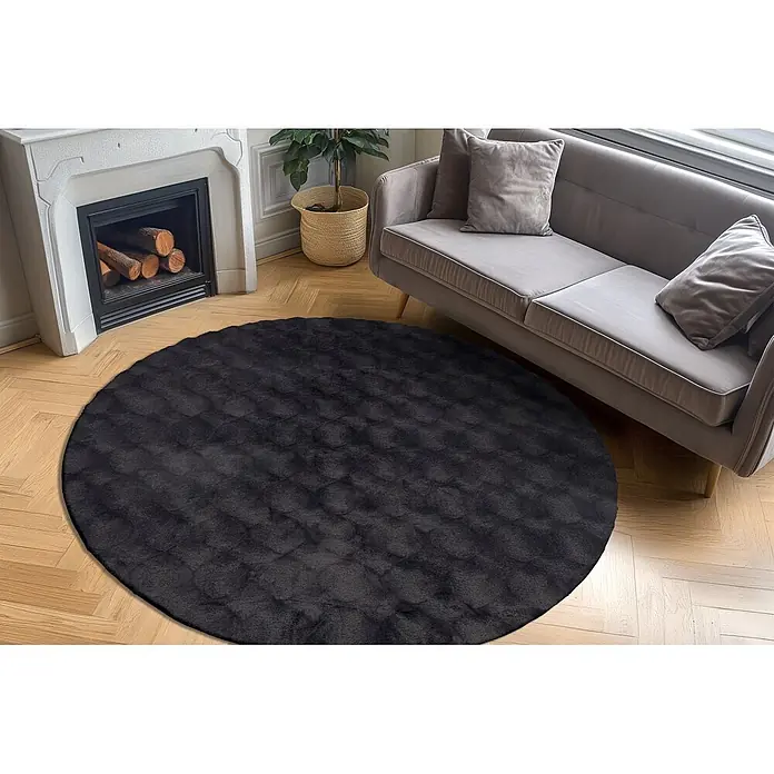 Kayoom Fellteppich Royal Glow 825 - Anthrazit, Durchmesser: 120 cm, 80 % Polyester, 20 % Baumwolle - Dunkelgrauer, runder Teppich mit weicher Textur. Liegt in einem Wohnzimmer vor einem Sofa und Kamin.
