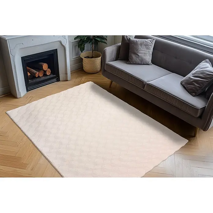 Kayoom Fellteppich Royal Glow 825 - Creme, 170 x 120 cm, 80 % Polyester, 20 % Baumwolle - Cremefarbener, strukturierter Teppich mit dezentem Muster, auf Holzboden in einem Wohnzimmer, teilweise unter einem grauen Sofa.