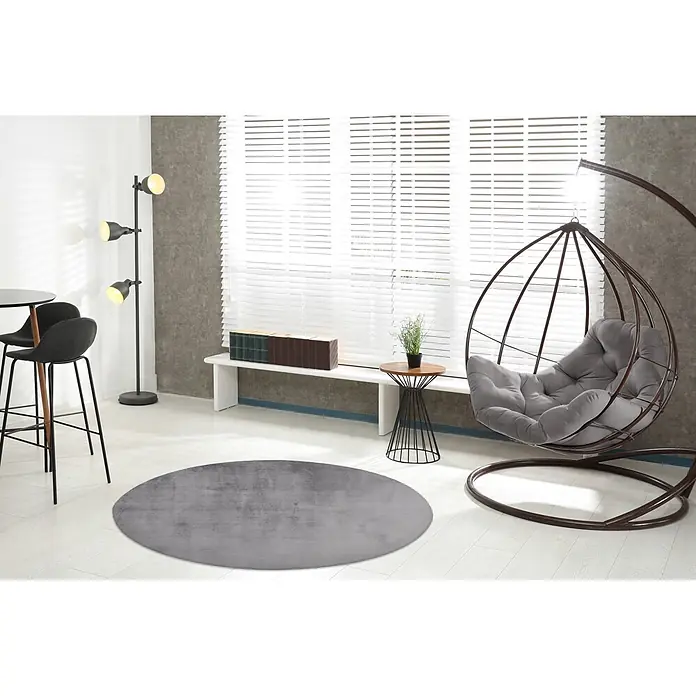 Kayoom Fellteppich Cross 425 - Silber, Durchmesser: 160 cm, 100 % Polyester - Moderner Wohnraum mit grauem Rundteppich, braunem Hängesessel mit grauem Kissen und schwarzer Stehlampe.