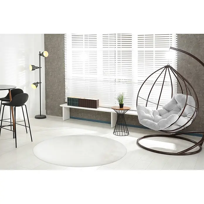 Kayoom Fellteppich Cross 425 - Weiß, Durchmesser: 160 cm, 100 % Polyester - Moderner Wohnraum mit braunem Hängesessel, weißer Bank, Bartisch mit Hockern und schwarzer Stehlampe am großen Fenster.
