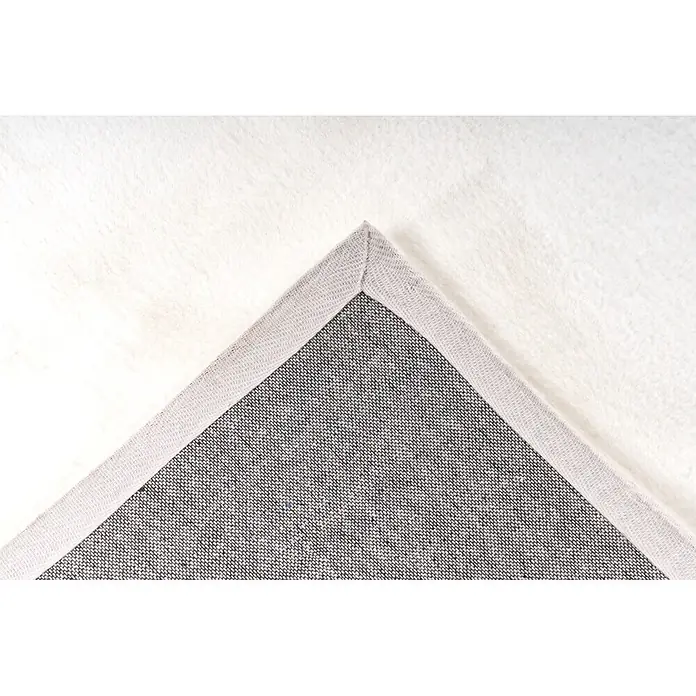 Kayoom Fellteppich Cross 425 - Weiß, 170 x 120 cm, 100 % Polyester - Detailaufnahme einer Teppichecke, die ihre weiße flauschige Oberfläche und graue gewebte Unterseite mit eingefassten Kanten zeigt.