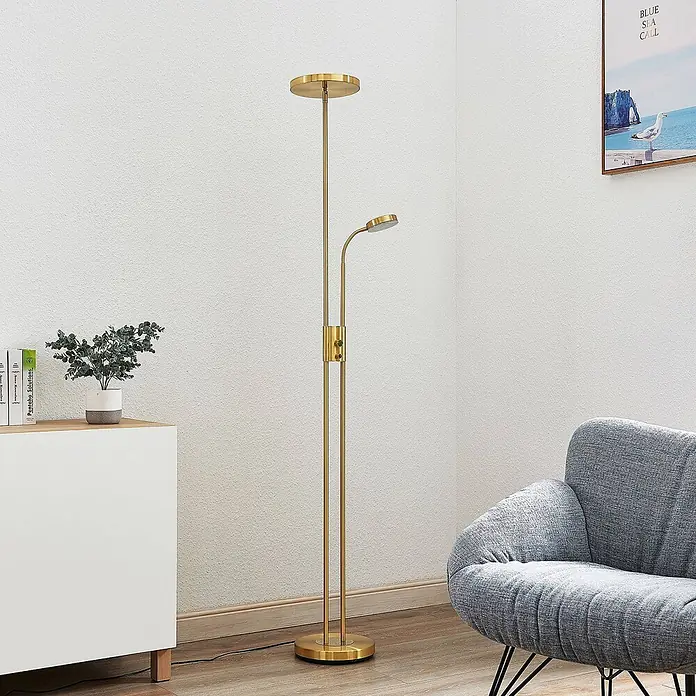 Lindby LED-Deckenfluter Seppa - messing / gold, messing / gold, Warmweiß - Goldene Stehlampe mit Deckenfluter und verstellbarer Leselampe, neben einem Sessel im Wohnzimmer.