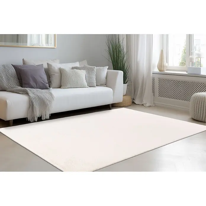 Kayoom Fellteppich Emperor 525 - Elfenbein, 290 x 200 cm, 100 % Polyester - Großer, weicher, cremeweißer Teppich auf hellem Holzboden in einem hellen Wohnzimmer, teilweise unter einem weißen Sofa.