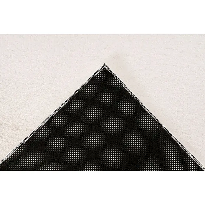 Kayoom Fellteppich Emperor 525 - Elfenbein, 290 x 200 cm, 100 % Polyester - Unterseite eines weißen flauschigen Teppichs mit schwarzer Anti-Rutsch-Rückseite, weißen Punkten und Zickzacknähten.
