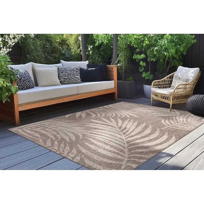 Kayoom Outdoor-Teppich Nibru 725 - Taupe, 290 x 200 cm, 100 % Polypropylen - Ein hellbrauner Outdoorteppich mit beigem Palmenblattmuster auf einer Holzterrasse unter Gartenmöbeln.