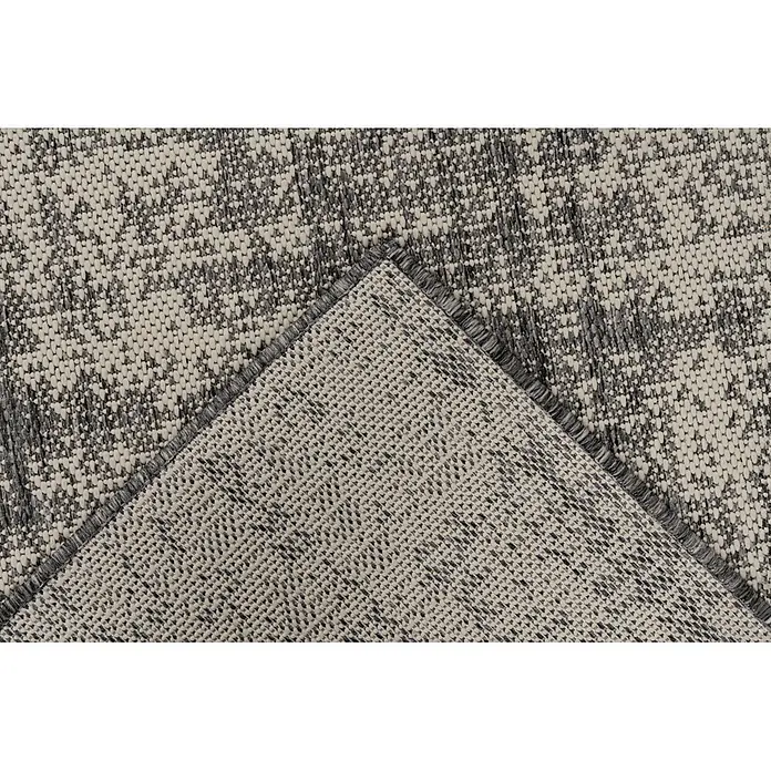 Kayoom Outdoor-Teppich Nibru 625 - Silber, 150 x 80 cm, 100 % Polypropylen - Nahaufnahme eines gewebten Teppichs in Grau- und Cremetönen, dessen Ecke die strukturierte Rückseite zeigt.