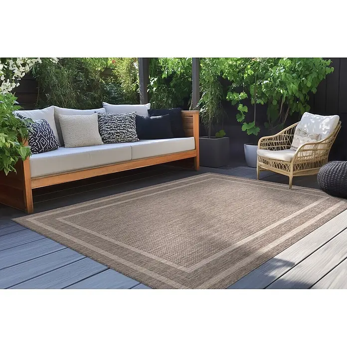 Kayoom Outdoor-Teppich Nibru 325 - Taupe, 110 x 60 cm, 100 % Polypropylen - Beiger Outdoorteppich mit Randmuster, auf einer Terrasse unter Gartenmöbeln.