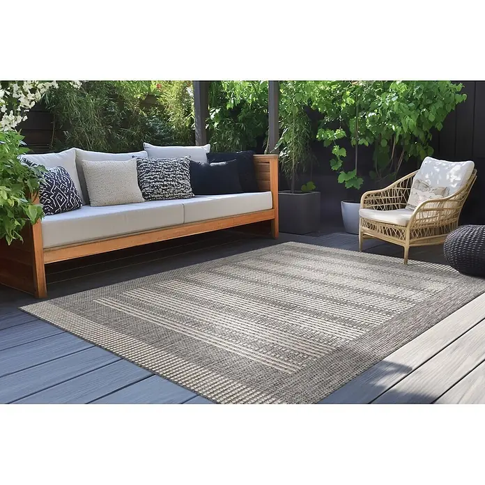 Kayoom Outdoor-Teppich Nibru 125 - Silber, 290 x 200 cm, 100 % Polypropylen - Grau-weiß gestreifter Outdoorteppich auf Holzdeck, ergänzt eine Terrassen-Sitzgruppe.