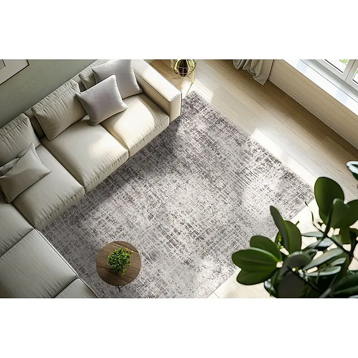 Kayoom Kurzflorteppich Amora 260 - Grau, 170 x 120 cm, 100 % Polyester - Ein hellgrauer Teppich mit abstraktem Muster auf hellem Holzfußboden im Wohnzimmer, teilweise unter einem Ecksofa.