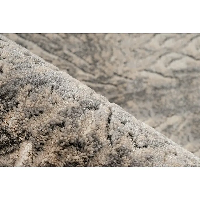 Kayoom Kurzflorteppich Adela 525 - Grau, 170 x 120 cm, 100 % Polypropylen - Nahaufnahme eines teilweise gerollten, texturierten Teppichs mit abstraktem Muster in Creme-, Beige-, Grau- und Dunkelgrautönen.