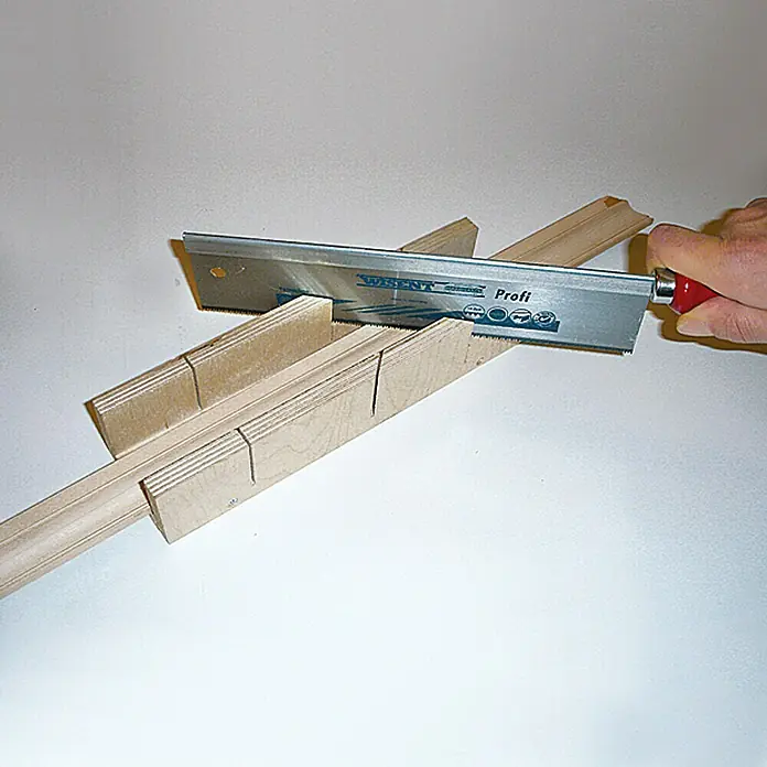 Wisent Sierra de tracción - Largo: 250 mm, Acero, Mango de madera, Reversible/Orientable - Una sierra de mano cortando una pieza de madera en una caja de ingletes, ideal para cortes de carpintería precisos.