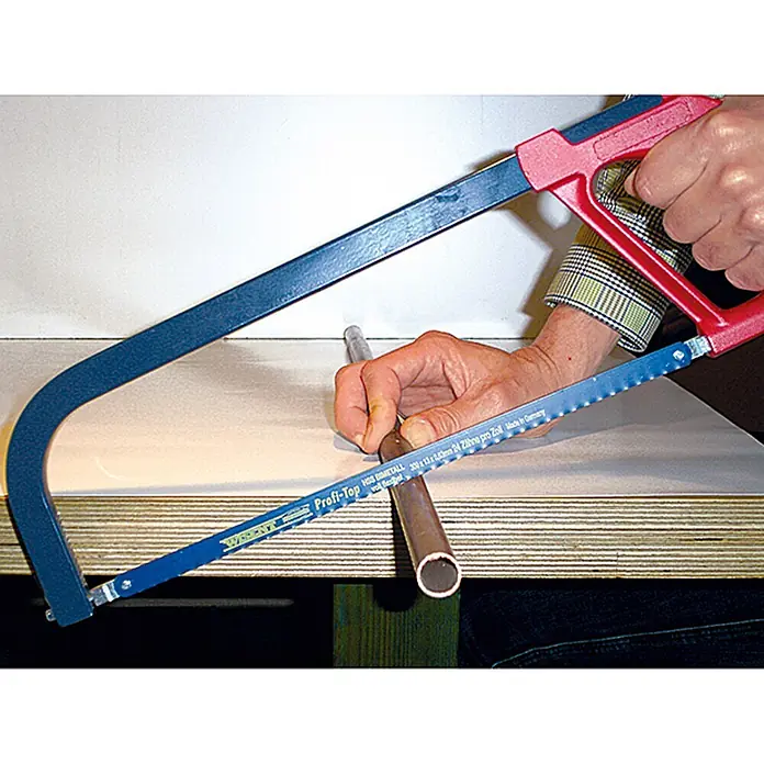 Wisent Sierra para metal - Largo: 300 mm, Acero - Persona usando una sierra para metales con hoja azul y mango rojo para cortar un tubo de cobre en un banco de trabajo.