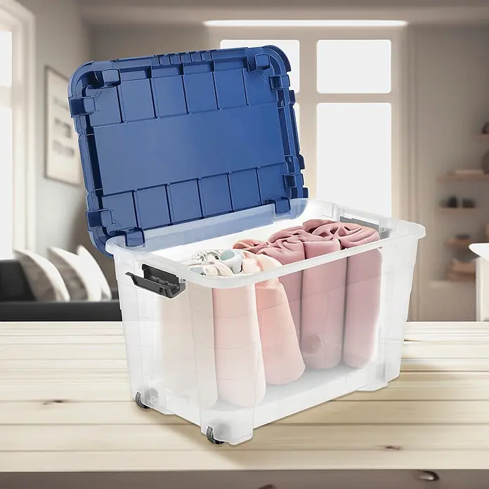 Aufbewahrungsbox 4UP - L x B x H: 59 x 39 x 36 cm, Transparent, Blau, Kunststoff - Transparente Plastik-Aufbewahrungsbox mit blauem Deckel und Rollen, gefüllt mit gerollten Stoffen. Auf einem Holztisch in einem Innenraum.