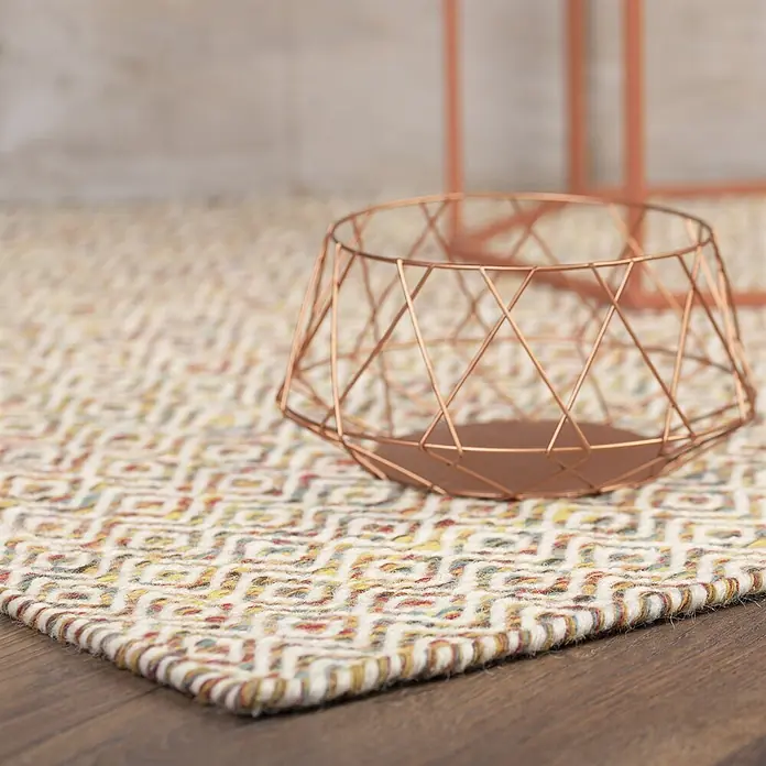 Kayoom Wollteppich Bombay 344 - Multi, 170 x 120 cm, 100 % Wolle - Ein roségoldener geometrischer Drahtkorb steht auf einem farbigen gemusterten Teppich.
