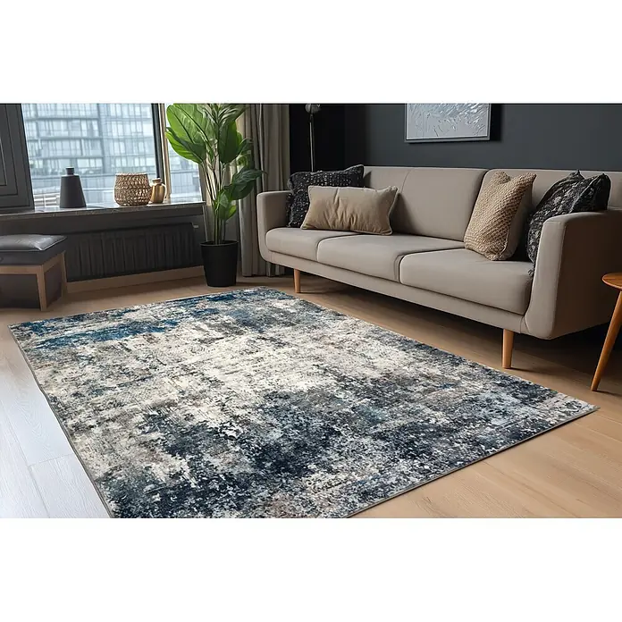 Kayoom Kurzflorteppich Elegantica 328 - Blau, 330 x 230 cm, 80 % Polyester, 20 % Baumwolle - Abstrakter Teppich in Blau, Grau und Weiß auf hellem Holzboden in modernem Wohnzimmer, teilweise unter beigem Sofa.