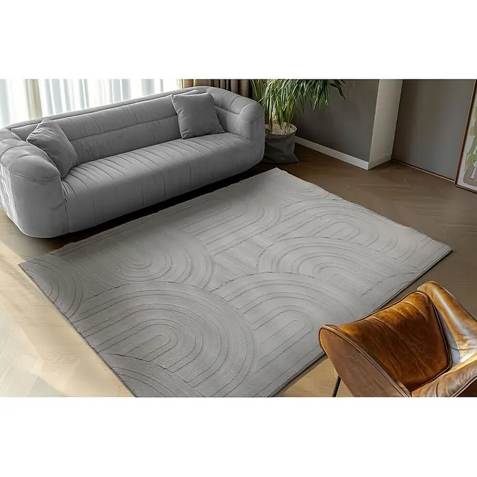 Kayoom Kurzflorteppich Cosmic 526 - Grau, 230 x 160 cm, 85 % Polyester, 15 % Wolle - Ein hellgrauer Teppich mit abstraktem Bogenmuster, der ein modernes Wohnzimmer unter Sofa und Sessel aufwertet.