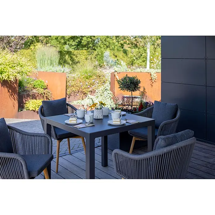 Bene Living Balkontisch Tarifa - Keramik-Tischplatte, Höhenverstellbar, Quadratisch, Anthrazit - Graues Outdoor-Esstisch-Set: Tisch und vier geflochtene Stühle mit dunklen Kissen. Auf einer Holzterrasse im Garten platziert.