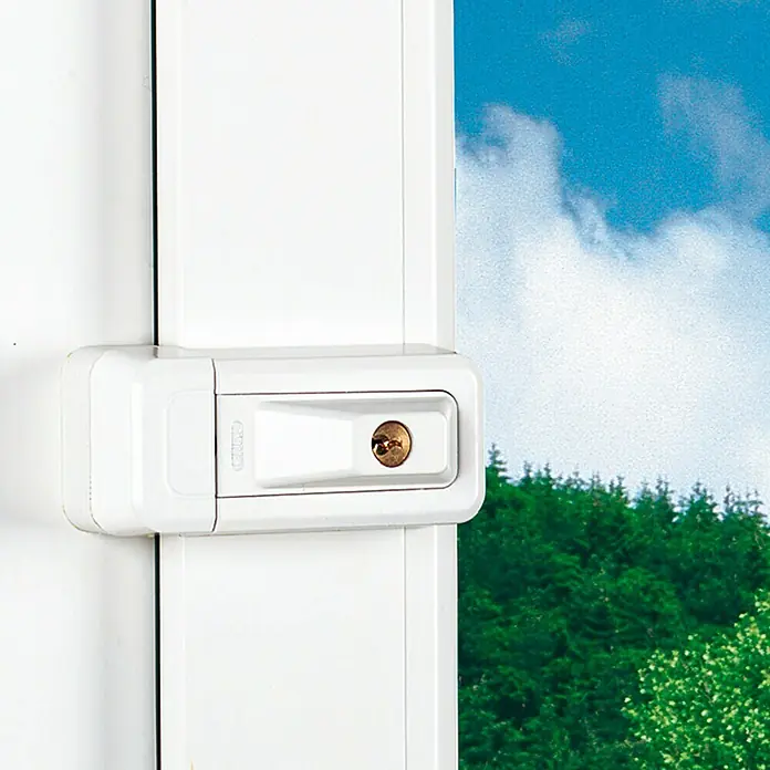 Abus Fenster-Zusatzschloss 3010 - DIN Anschlag: Universell einsetzbar, Weiß - Nahaufnahme eines weißen Fensterverschlusses mit goldenem Schloss vor einer Landschaft mit Bäumen und blauem Himmel.
