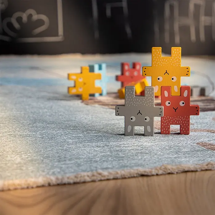 Kayoom Kinderteppich Joanna 611 - Multi, 170 x 115 cm, 70 % Baumwolle, 30 % Polyester - Bunte Holz-Tierpuzzle-Teile für Kinder, auf einem gemusterten Teppich gestapelt.