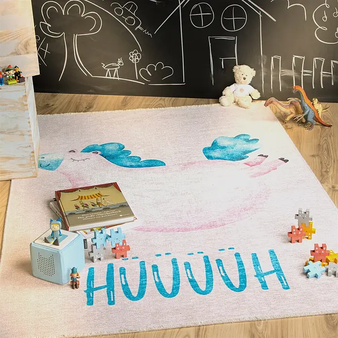 Kayoom Kinderteppich Joanna 625 - Multi, 170 x 115 cm, 70 % Baumwolle, 30 % Polyester - Ein hellrosa Kinderteppich mit blauem Einhorn und dem Wort 'HUUUUH' in einer verspielten Kinderzimmerumgebung.