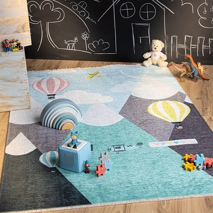 Kayoom Kinderteppich Joanna 615 - Multi, 170 x 115 cm, 70 % Baumwolle, 30 % Polyester - Kinderteppich mit verspieltem Berg- und Heißluftballon-Landschaftsdesign, umgeben von Spielzeug in einem Kinderzimmer.