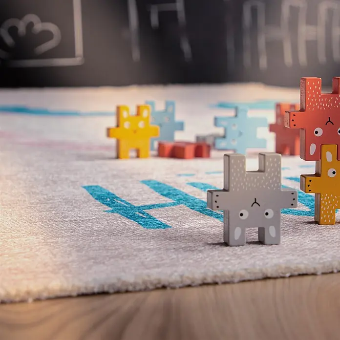 Kayoom Kinderteppich Joanna 625 - Multi, 170 x 115 cm, 70 % Baumwolle, 30 % Polyester - Bunte Holz-Tierpuzzle-Teile, teils gestapelt, teils stehend, auf hellem Teppich mit blauem Text.