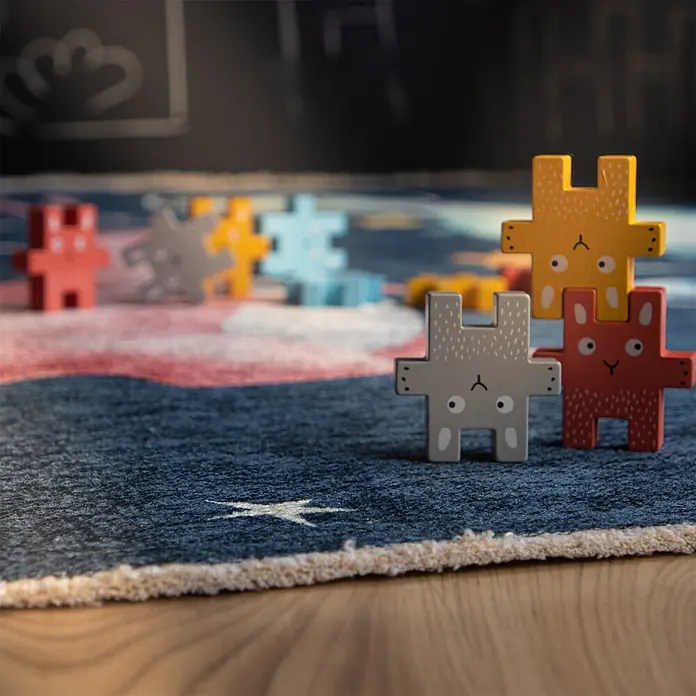 Kayoom Kinderteppich Joanna 627 - Multi, 170 x 115 cm, 70 % Baumwolle, 30 % Polyester - Bunte Holz-Tierpuzzle-Teile in Rot, Grau, Gelb und Blau, teils gestapelt, teils auf einem blau-rot gemusterten Teppich verteilt.