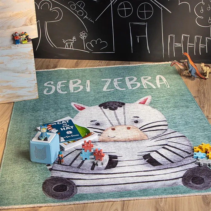 Kayoom Kinderteppich Joanna 624 - Multi, 170 x 115 cm, 70 % Baumwolle, 30 % Polyester - Kinderteppich in Grün mit großer, freundlicher Zebra-Illustration und 'SEBI ZEBRA'-Schriftzug, umgeben von Spielzeug in einem Kinderzimmer.
