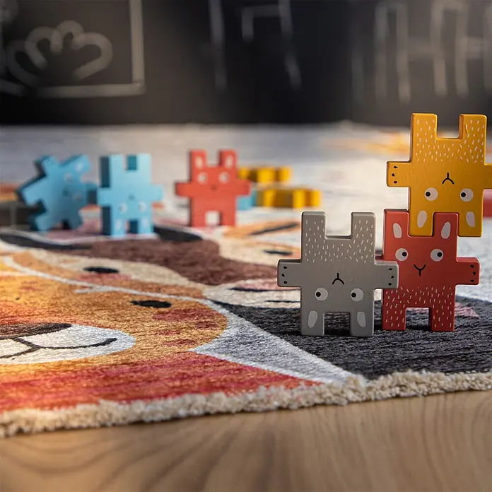 Kayoom Kinderteppich Joanna 616 - Multi, 170 x 115 cm, 70 % Baumwolle, 30 % Polyester - Bunte Tier-Holz-Puzzleteile, teilweise gestapelt, auf einem gemusterten Teppich.