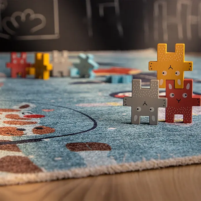 Kayoom Kinderteppich Joanna 610 - Spaceblau, 170 x 115 cm, 70 % Baumwolle, 30 % Polyester - Bunte Holz-Tier-Puzzleteile auf einem blauen Teppich gestapelt.