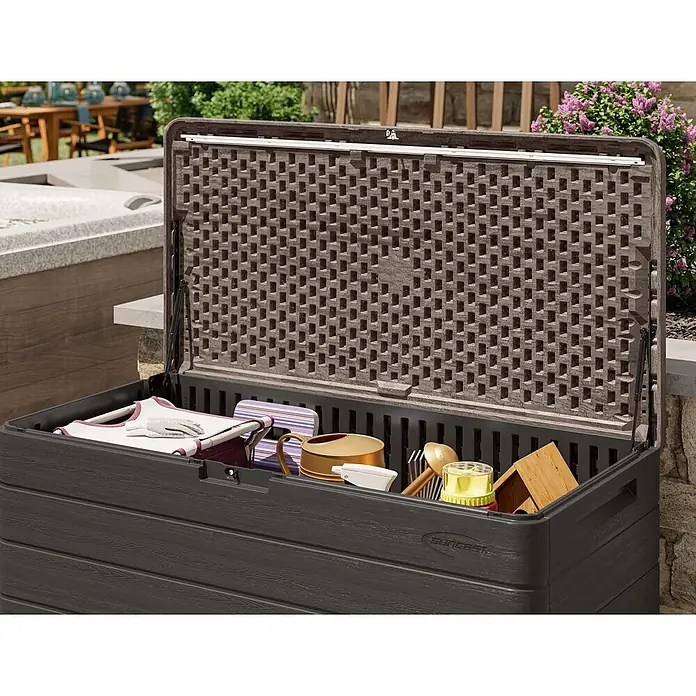 Suncast Auflagenbox - 147 x 74 x 74 cm, Kunststoff, Anthrazit - Dunkelbraune Garten-Aufbewahrungsbox in Holzoptik, geöffnet auf einer Terrasse, gefüllt mit Gartenwerkzeugen.