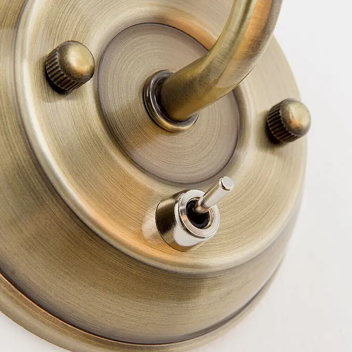 Orion Leuchten Wandleuchte MAJA -  - Detailaufnahme einer messingfarbenen Metallbasis mit gebogenem Arm, zwei Rändelschrauben und einem Chrom-Kippschalter.