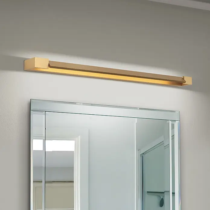Orion Leuchten Spiegelleuchte - 24 W, L x B x H: 10 x 90 x 4,2 cm - Goldfarbene lineare LED-Spiegelleuchte über einem Badspiegel, die warmes Licht nach unten wirft.