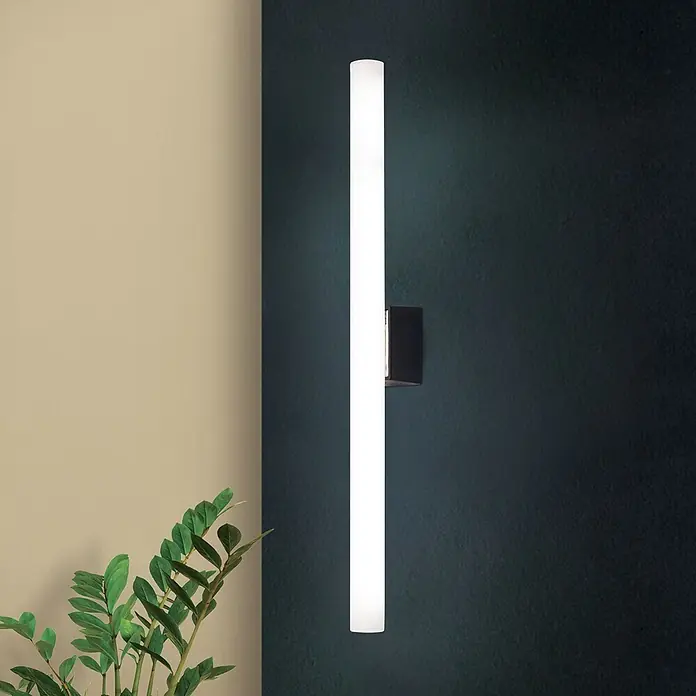 Orion Leuchten Wandleuchte - 60 W, L x B x H: 7 x 50 x 3,8 cm, S14d - Weiße lineare LED-Wandleuchte vertikal an dunkler Wand montiert, beleuchtet den Bereich. Eine Pflanze ist im Vordergrund sichtbar.