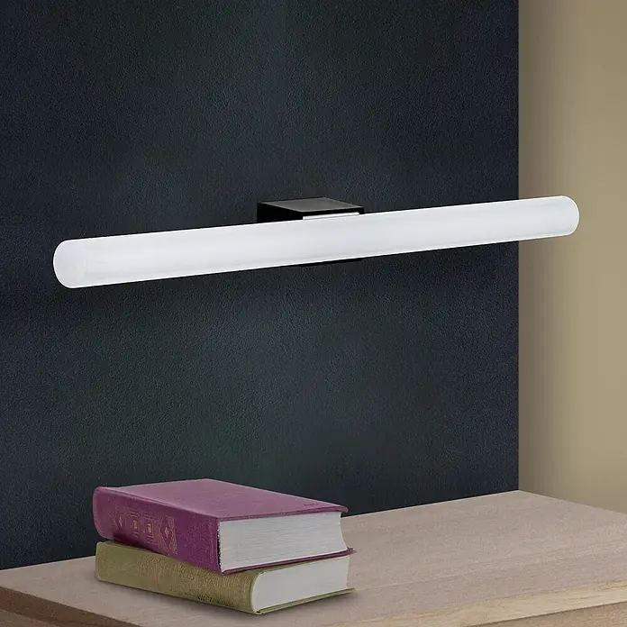 Orion Leuchten Wandleuchte - 60 W, L x B x H: 7 x 50 x 3,8 cm, S14d - Lineare LED-Spiegelleuchte mit mattweißer Röhre und schwarzem Sockel, an dunkler Wand über Büchern auf Holzfläche montiert.